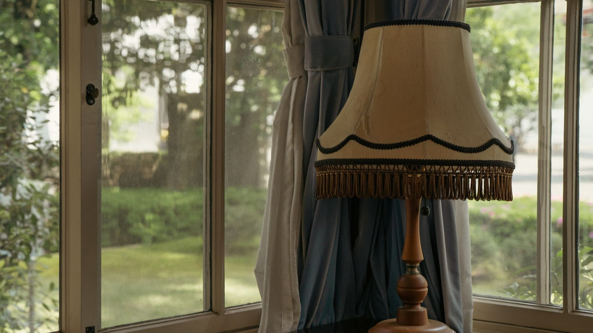 Lampe vintage à abat-jour frangé devant une fenêtre aux rideaux épais