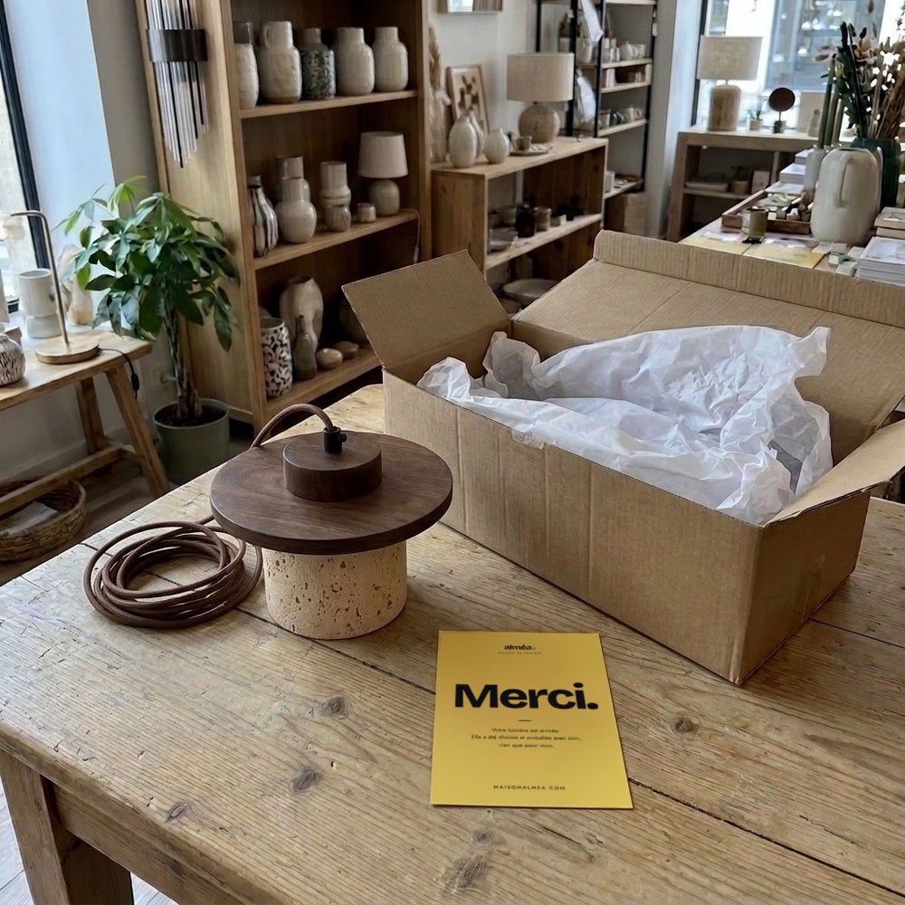 Suspension travertin et bois, déballée sur la table de la boutique avec la carte Merci