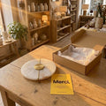 Applique en albâtre et laiton doré de 20 cm posée sur une table de boutique, à côté de son carton et de la carte Merci #or